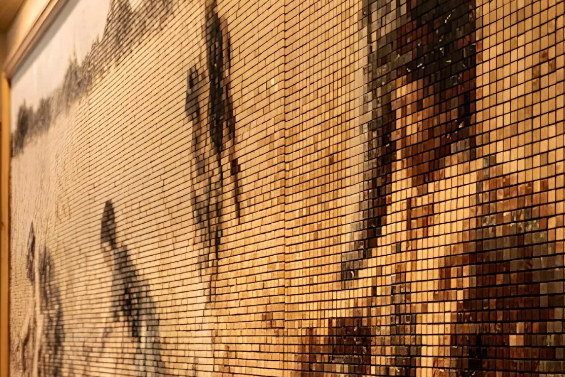 A close view of the same mosaic under raking light: individual one-centimetre stones read one by one, the picture resolving into a grid of warm ochre, cream and near-black tesserae.