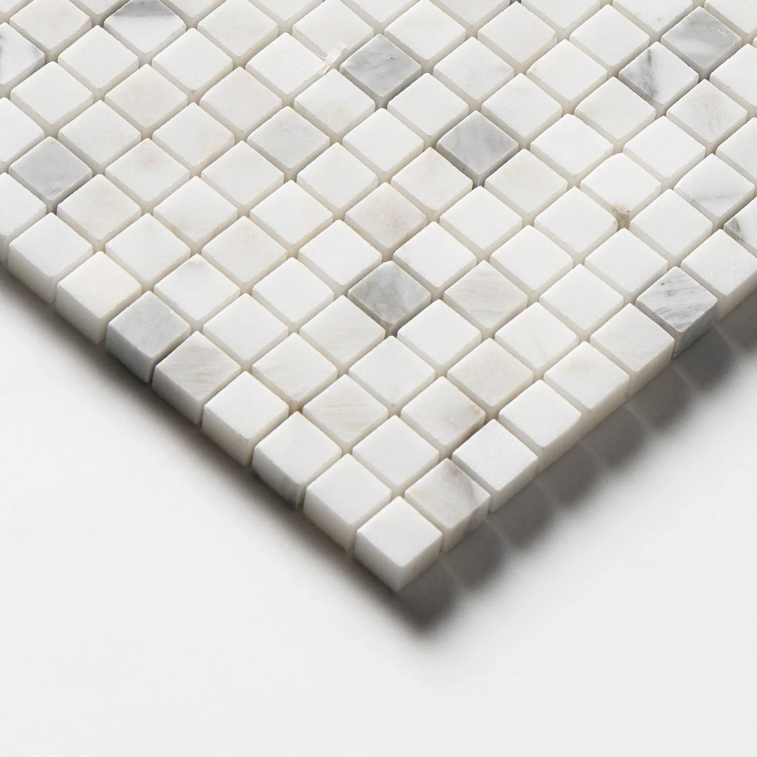 Corner detail of the honed Calacatta Gold mosaic, angled to show the cut edge and the depth of the individual square chips.