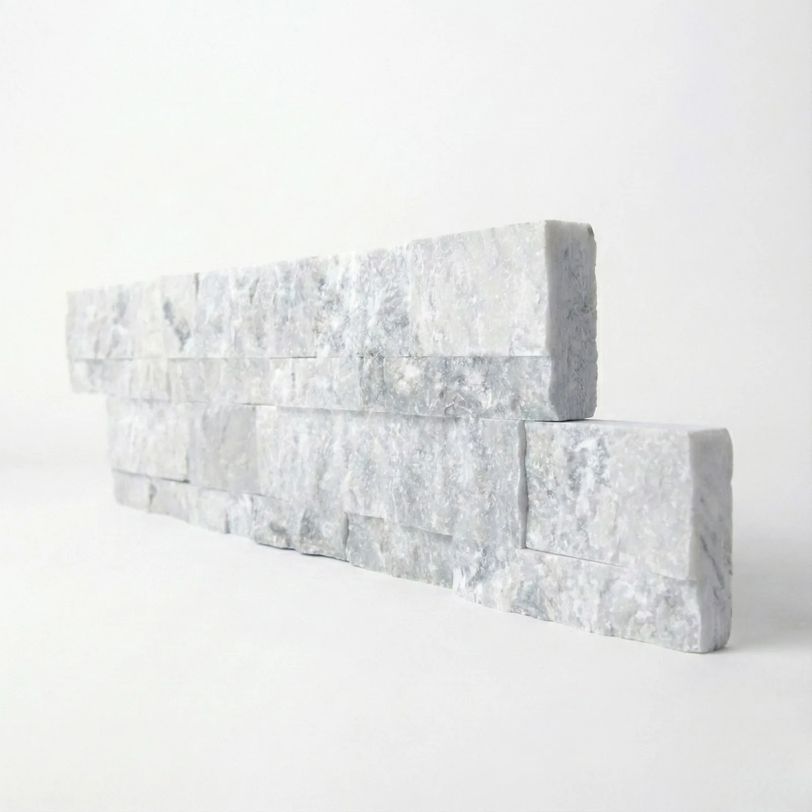Two courses of Tundra Grey marble ledger panel on a pale studio ground, grey and white mottling across the split faces.