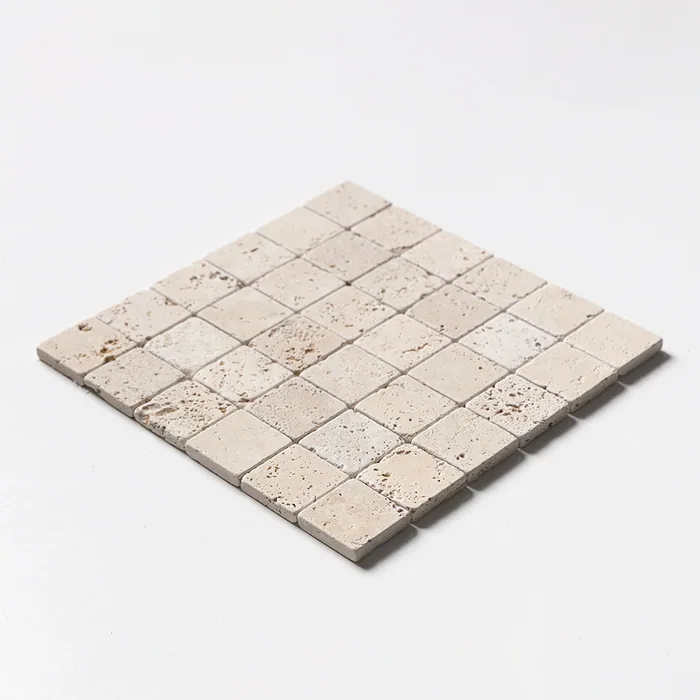 Ivory travertine mosaic of two-inch tumbled squares, the sheet angled to show its softened edges and warm cream tone.