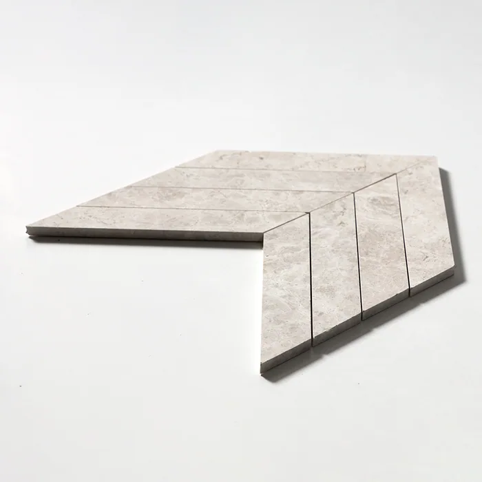 A large chevron of pale grey Silver Shadow marble, the arrow-shaped sheet tilted so the sharply mitred joints and the cut edge of the stone catch the light.
