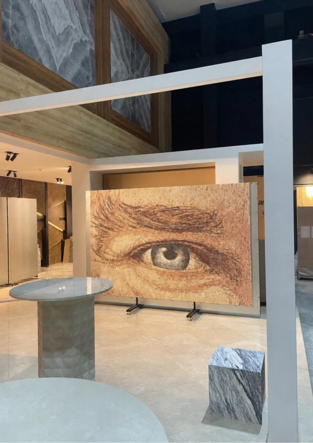 The finished eye study installed on a wall, a single monumental eye and brow built in rust and sepia tesserae over a warm cream ground.