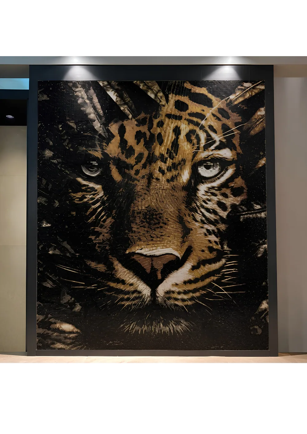 The finished leopard mosaic hung in a dark frame on an interior wall, washed by two ceiling downlights that rake across the surface so the gold tesserae flare and the black ground stays deep.