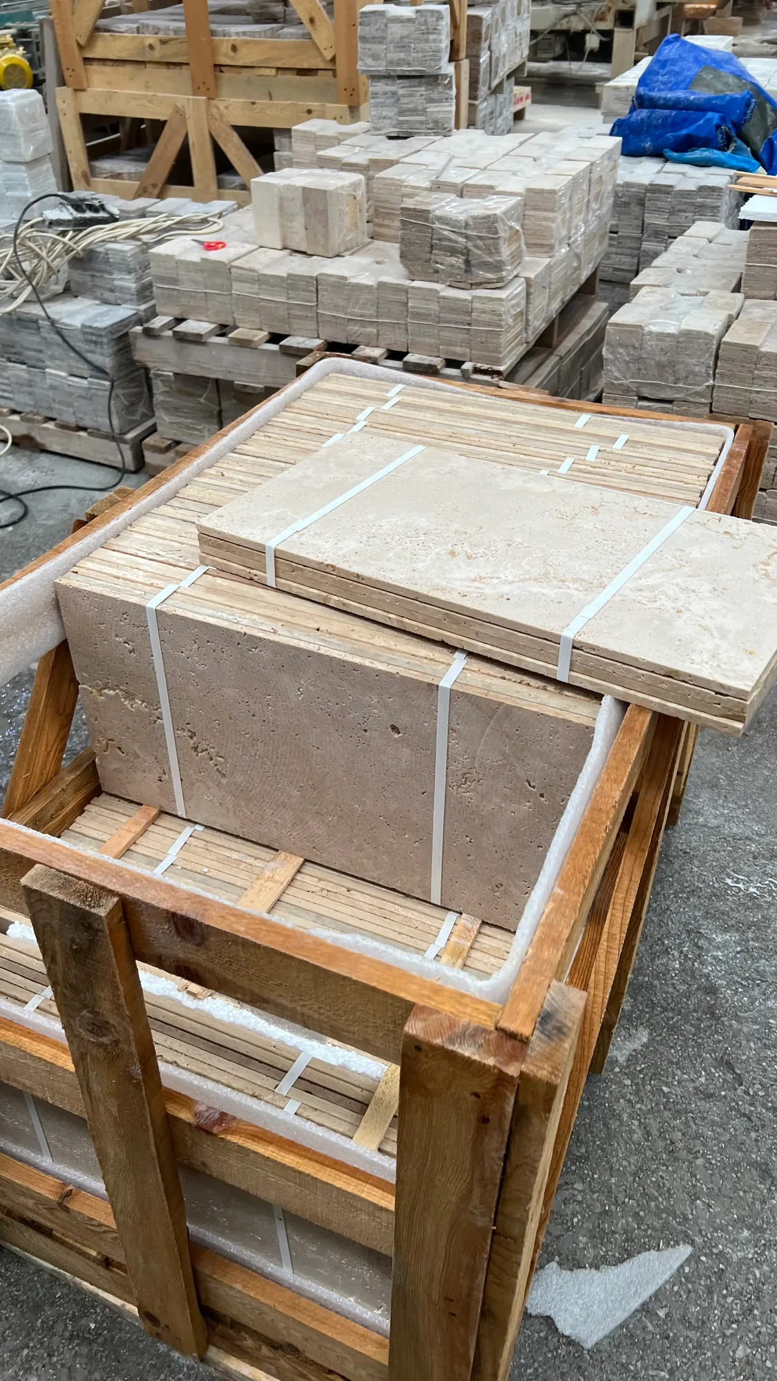 Crated travertine strapped onto timber pallets in the warehouse, banded slabs and cut stock stacked on pallets receding behind it down the aisle.
