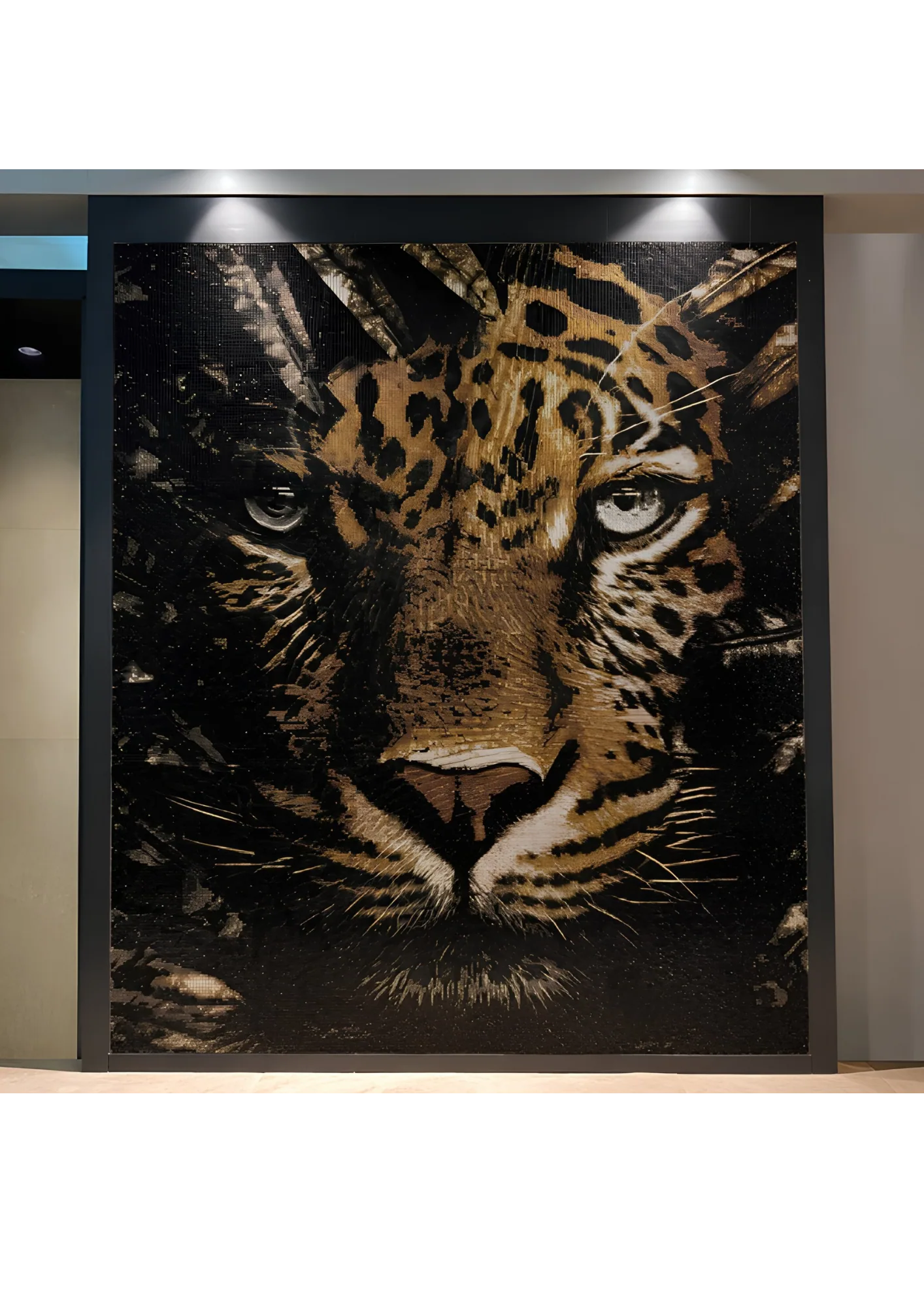 The finished mosaic photographed in place: the leopard panel hung in a dark frame on an interior wall, washed by two ceiling downlights that rake across the surface so the gold tesserae flare and the black ground stays deep.